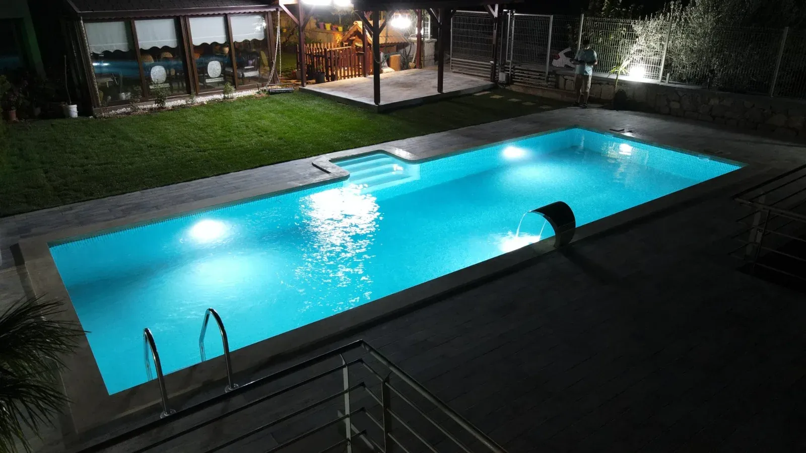 Gece aydınlatmalı bahçe havuzu, paslanmaz su perdesi ve ahşap deck